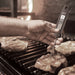 Bios DT134 digital folding pocket thermometer in use, hand inserting the probe into a steak on a barbecue grill