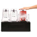 Blendtec JRE-612 blender jar rinsing station in use, hand pressing a jar down to rinse it beside two other jars