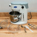 Globe SP05 5 qt planetary mixer on a butcher block counter with whisk, dough hook, beater and bowl guard