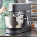 Hamilton Beach CPM800 commercial planetary stand mixer in use in a bakery, baker adding flour to the steel bowl