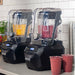 Two Hamilton Beach HBH855 Summit high performance blenders blending smoothies on a cafe counter with cups