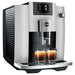 Jura E6 residential automatic coffee machine in platinum, angled left view showing ribbed side and two espressos