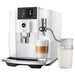 Jura glass milk carafe for automatic coffee machines, 16.9 oz, beside a white Jura coffee machine making a latte