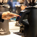 MACAP SUPRA 68 G Series coffee grinder in use in a cafe, barista pressing the touchscreen to select a dose