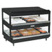 Nemco 6480 series heated pass through station, black finish with slanted shelves stocked with packaged hot food