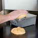 Nemco 8150 series butter spreader in use, hand pressing a sliced bun onto the roller to butter it, stainless steel