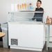Nordic Air IDF-47 white ice cream dipping freezer in use, server holding a scooped ice cream cone behind the case