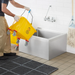 Phoenix MS-2024-10 stainless steel mop sink in use, worker emptying a yellow mop bucket into the bowl under a faucet