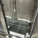 Open box Nordic Air SR-54 refrigerator interior, close-up of the wrapped wire shelves on the floor by the door hinge