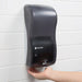 San Jamar SH900TBK black touchless hand soap dispenser mounted on a white tiled wall, dispensing soap into a hand