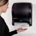 San Jamar T8400TBK black compact touchless paper towel dispenser mounted on a tiled wall with a hand under the sensor