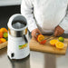 Waring JC4000 high powered citrus juicer in white shown in use as a chef halves oranges on a cutting board