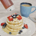 FIFO squeeze bottle in use, drizzling syrup over a stack of waffles topped with berries and banana slices