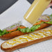 FIFO squeeze bottle in use, dispensing mustard sauce onto a long sub sandwich on a white tiled surface