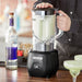 Hamilton Beach HBB908R 44 oz bar blender in use on a bar counter, bartender holding the container of margaritas