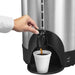 Hamilton Beach HCU100S 100 cup coffee/tea percolator, close-up of hand using the tap to dispense into a foam cup