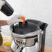 Hamilton Beach HJE960 commercial electric juicer in use, gloved hand feeding a carrot into the top feed chute