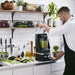 KitchenAid KSBC1B2BM commercial blender with sound enclosure in use by a chef making a green smoothie