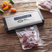 LEM 1379 MaxVac 100 out of chamber vacuum sealer in use, sealing a bag of meat on a wooden table with peppers