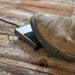 LEM 724 grinder foot switch shown in use, a work boot pressing the black foot pedal on a rustic wooden floor