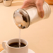 Winco 12 oz glass sugar pourer shown in use pouring sugar into a white cup of coffee