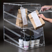Winco ADC-4 four tier clear acrylic display case used as a takeout pickup station with bags and coffee cups