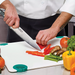 Winco Acero 8 inch chef's knife shown in use by a chef slicing red peppers on a cutting board