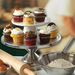 Winco metal cake stands stacked in tiers and displaying cupcakes on a bakery counter with baking supplies