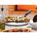 Winco pizza server with handle shown in use, serving slices of vegetable pizza from a pan beside a brick oven