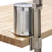 Winco standard steel manual can opener clamped to a wooden butcher block counter while opening a large tin can
